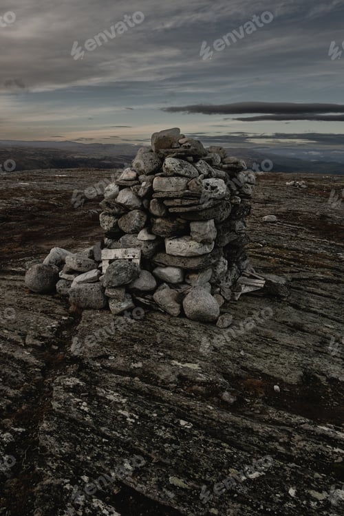 Preview: dark moody landscape cairn stack of stones on top of a mountain at dusk