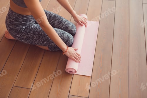 Preview: Woman Rolling Up Yoga Mat on Wooden Floor
