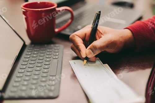 Preview: African American man sitting at home office desk writing out a check with a pen