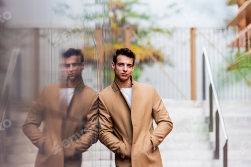 Preview: Portrait of stylish handsome young man with coat standing outdoors and leaning on wall.