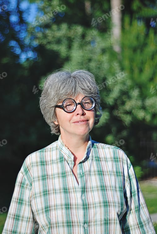 Preview: Seniors woman in round eyeglasses against green backdrop,outdoor