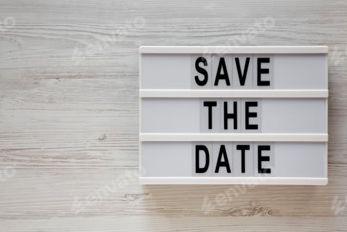 Preview: 'Save the date' words on a lightbox on a white wooden surface, top view.
