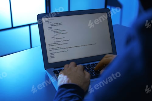 Preview: Man using laptop at table in dark room, closeup. Criminal offence
