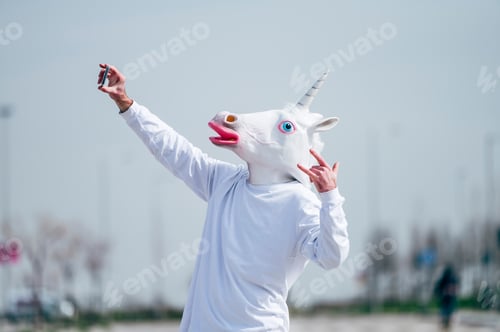 Preview: Man wearing unicorn mask taking a photo with smartphone