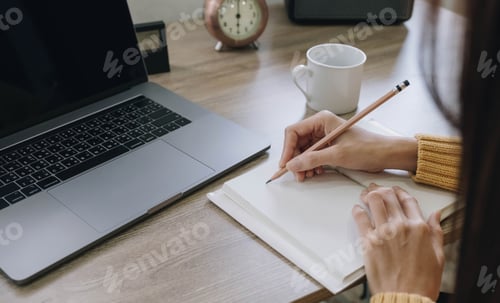 Preview: Beautiful woman writing taking notes while sitting in front her computer laptop at the wooden