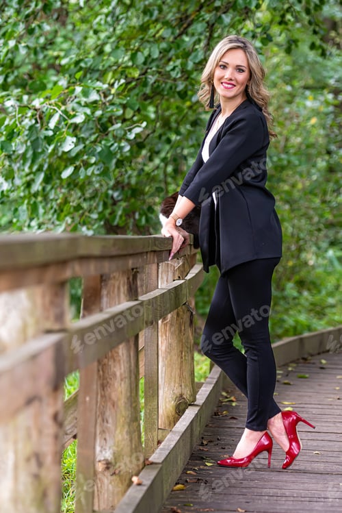 Preview: young blonde woman standing near wooden railings in park