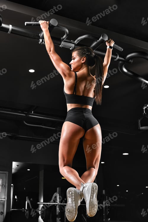 Preview: Sexy young fitness girl pulls up in the gym. Brunette fitness woman in black sportswear with perfect