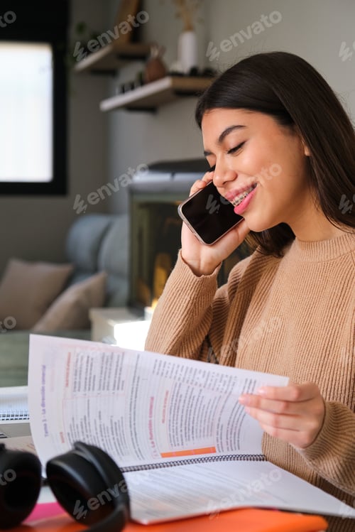Preview: Female college student with braces talking on the phone while study at home.
