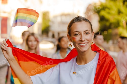 Preview: Young lesbian woman wrapped in rainbow flag smiling during pride parade