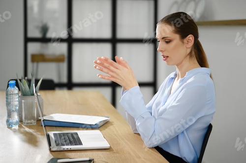 Preview: Professional woman engaged in a video call while seated at a wooden desk in an office setting