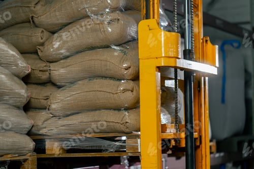 Preview: close up a worker at a coffee factory uses a yellow forklift to lift and place a pallet on shelf