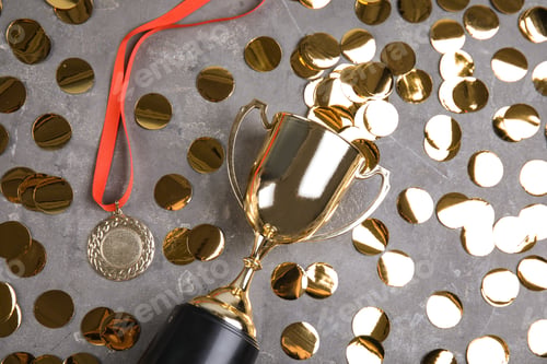 Preview: Gold trophy cup, medal and confetti on grey stone background, flat lay