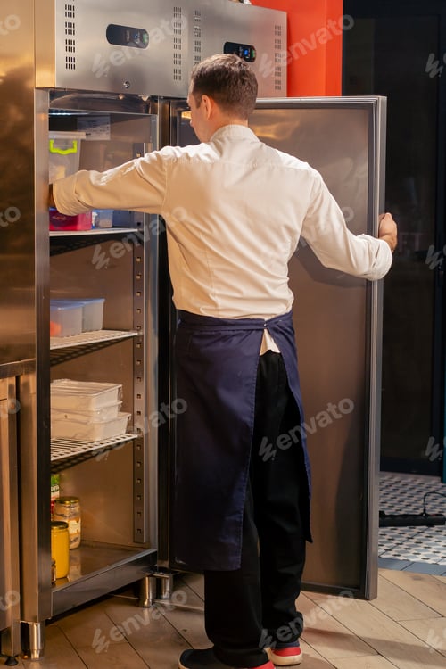 Preview: professional kitchen chef looks into the fridge and chooses ingredients for cooking food concept