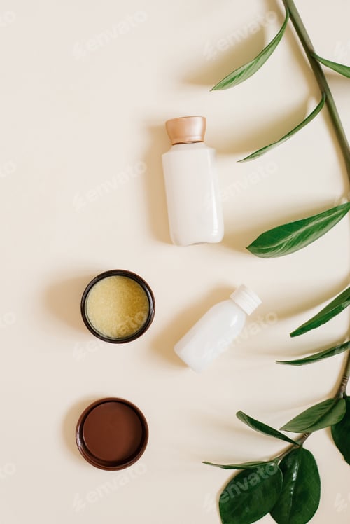 Preview: Bottles with Body or Face Cream, Solid Cocoa Butter in an Open Jar and Branch of Tropical Plant
