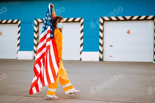 Preview: American woman with medical face mask posing with american flag. Covid-2019.