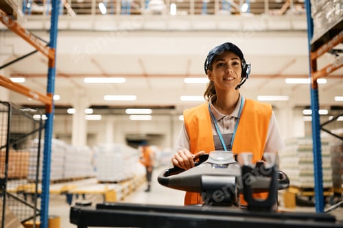 Preview: Young female worker driving pallet jack while working at distribution warehouse.