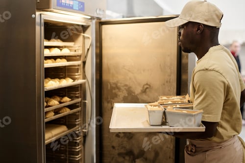 Preview: Young Black man putting fresh pastries in freezer at bakery kitchen