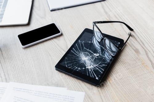 Preview: Eyeglasses on smashed digital tablet near documents and digital devices on wooden background
