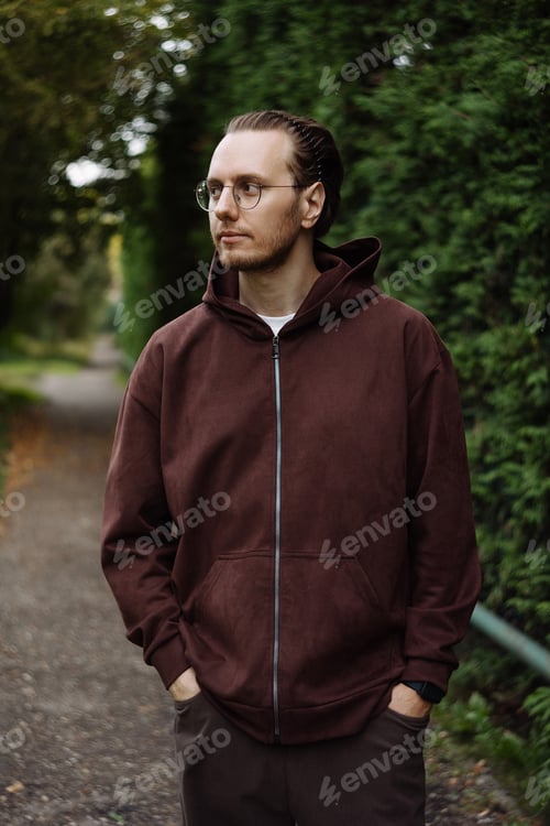Preview: Young man in brown hoodie standing on park path