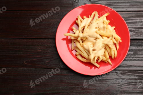 Preview: Delicious french fries with cheese sauce on wooden table, top view. Space for text