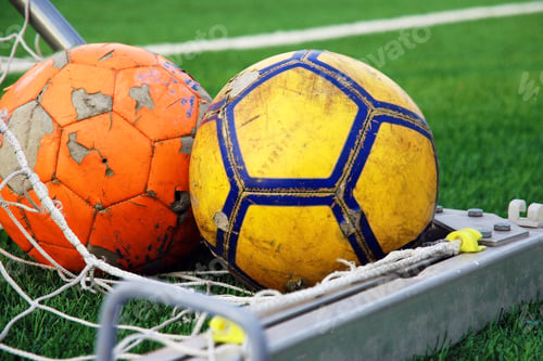Preview: Two ragged soccer football balls lying in the corner of the goal against green football field
