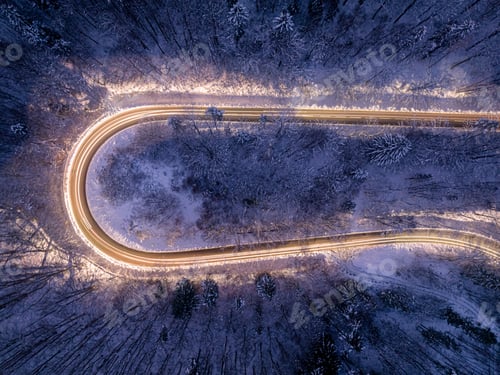 Preview: Car headlights illuminating a winding winter road after dark.
