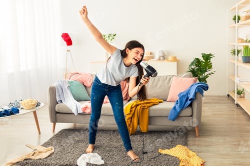 Preview: Full length of Indian teenage girl dancing and singing in messy room, using blowdryer as mic, having