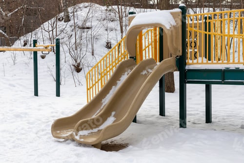 Preview: Playground slide in park without kids, covered with snow in winter season