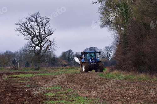 Preview: Agricultural tractor operating in a misty, rural area next to a forest
