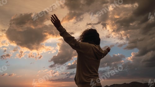 Preview: Back view of a female standing under the cloudy sunset sky with hands up