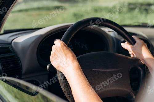 Preview: Close-up of female hands on the steering wheel of a car. Senior woman driver in car, cropped image