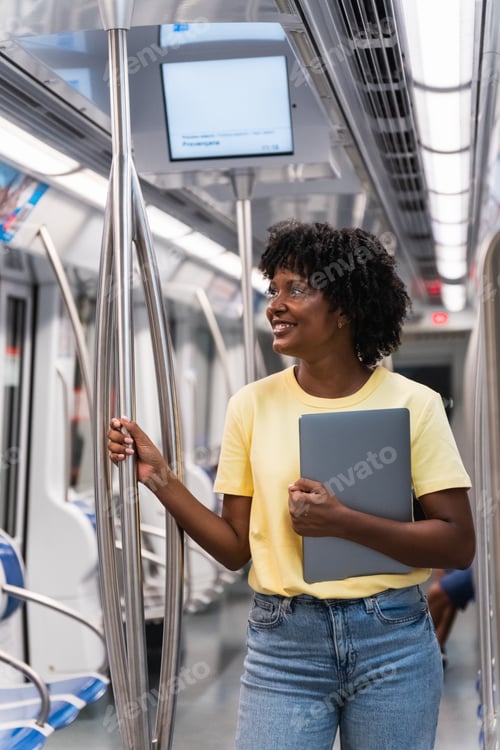 Preview: Smiling student standing with laptop in subway train
