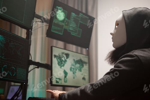 Preview: Masked hacker with a hoodie using computer to plan a massive cyber attack