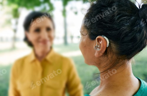 Preview: Adult woman with a hearing impairment uses a hearing aid to communicate with her female friend at