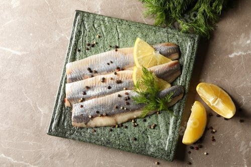 Preview: Plate with herring fish slices and spices on gray background