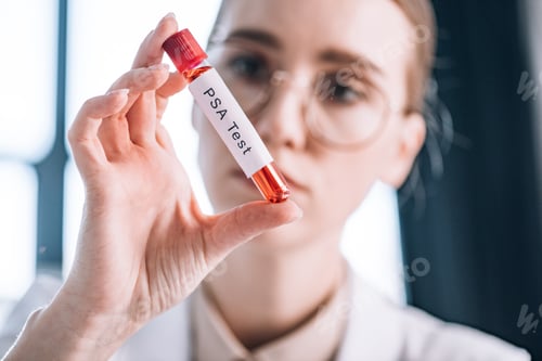 Preview: selective focus of attractive immunologist in glasses looking at test tube with psa test letters