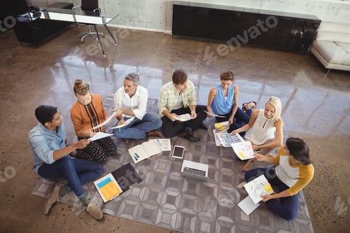 Preview: Business people working while sitting on floor in creative office
