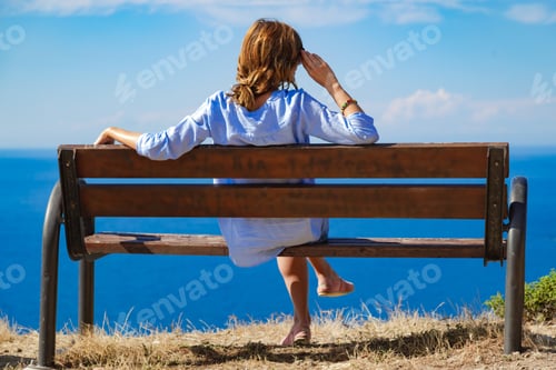 Preview: Woman Sitting On A Cliff Bench Above Ocean / Sea.