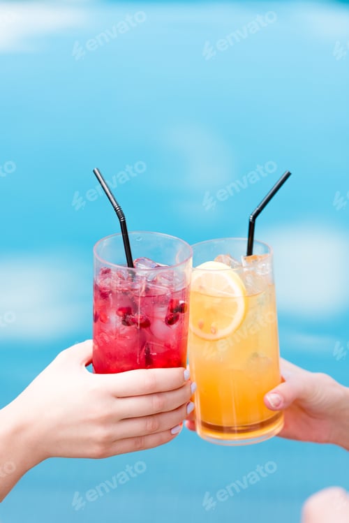 Preview: cropped shot of women clinking glasses of cocktails in front of swimming pool