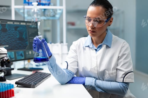 Preview: Biologist researcher holding transparent glassware analyzing blue solution