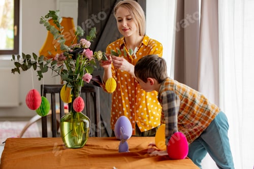 Preview: mother and son are decorating a table with paper eggs for Easter. Indoor