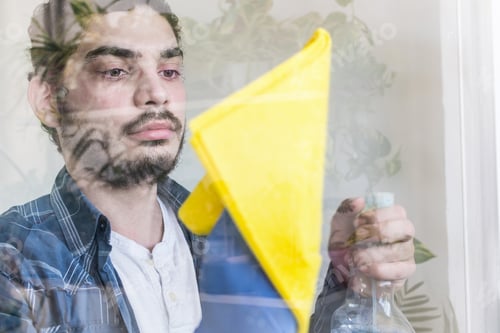 Preview: Adult male cleaning a window with a yellow cloth and chemicals
