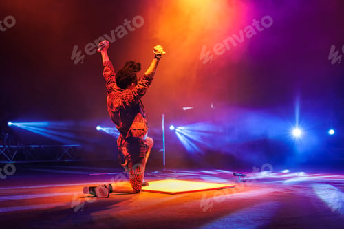 Preview: Clown with a funny hairstyle entertains guests in the circus arena in light of spotlights and smoke
