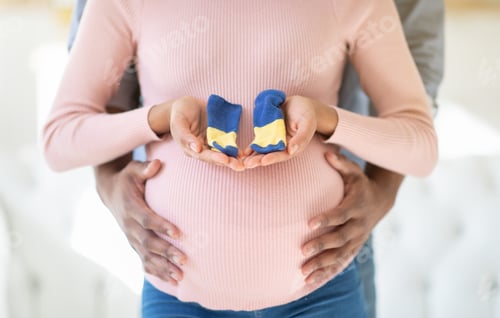 Preview: Cropped view of black pregnant woman and her husband with tiny baby socks, closeup