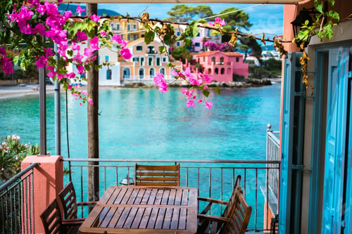 Preview: Lilac fuchsia blossom flower over hotel veranda in front of turquoise colored bay of Mediterranean