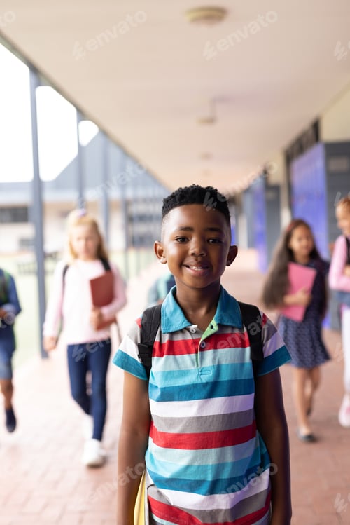 Preview: Vertical portrait of smiling african american boy in elementary school corridor, with copy space