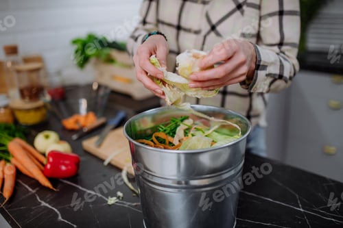 Preview: Woman throwing vegetable cuttings in a compost bucket in kitchen