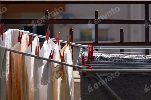 Preview: Close up of outspread clothes on indoor folding clothes in balcony with red pins under sunlight