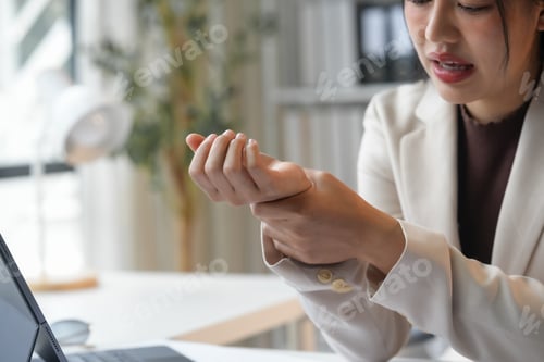 Preview: Young businesswoman experiencing wrist pain while working at her desk