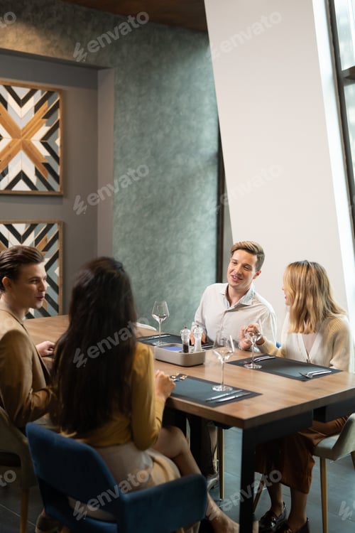Preview: Two young cheerful couples in smart casualwear having dinner in restaurant